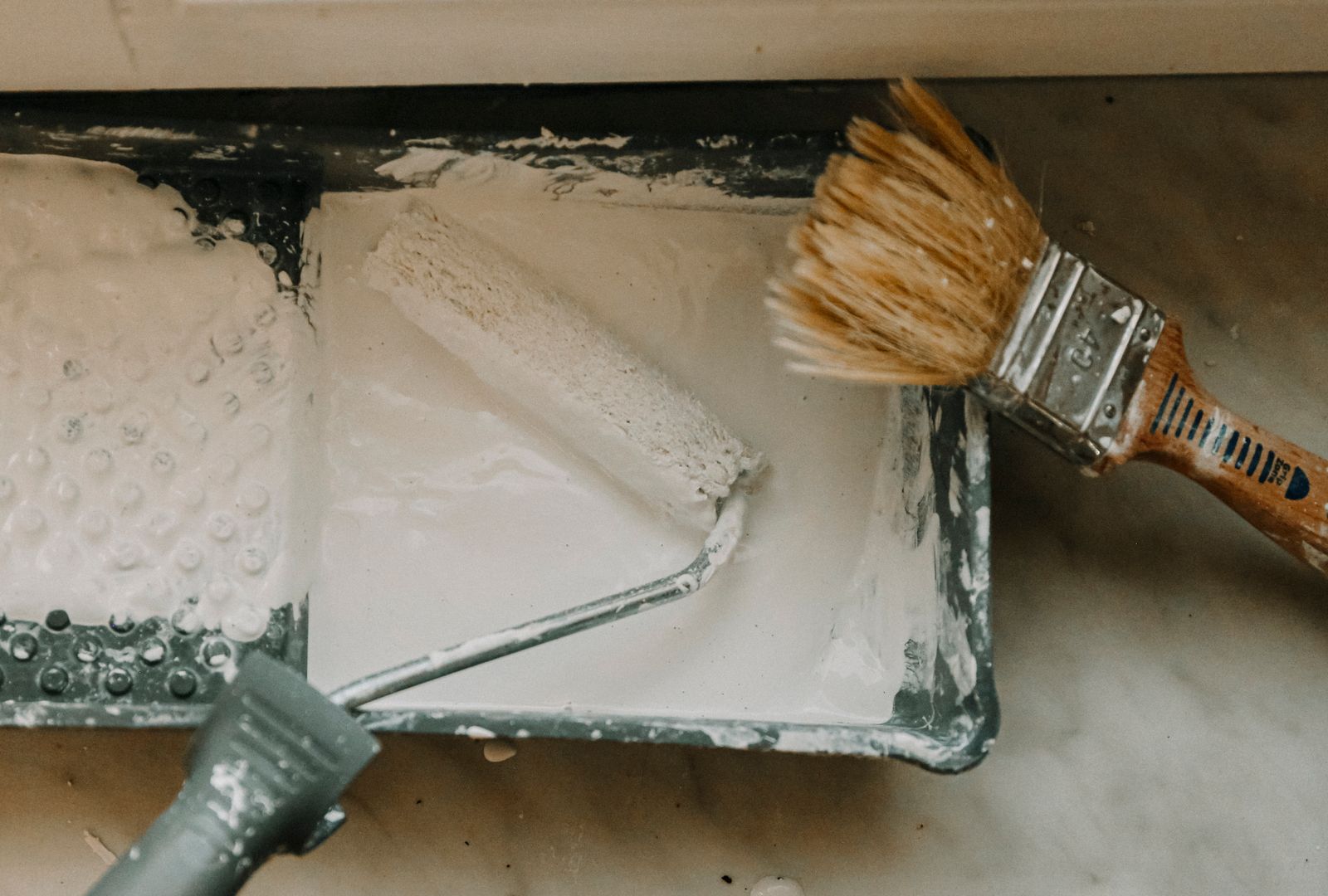 Paint roller and brushes resting in a tray of white paint
