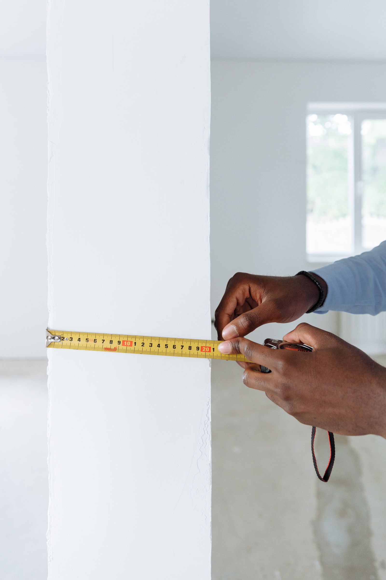 Hands holding a yellow tape measure against a white interior wall