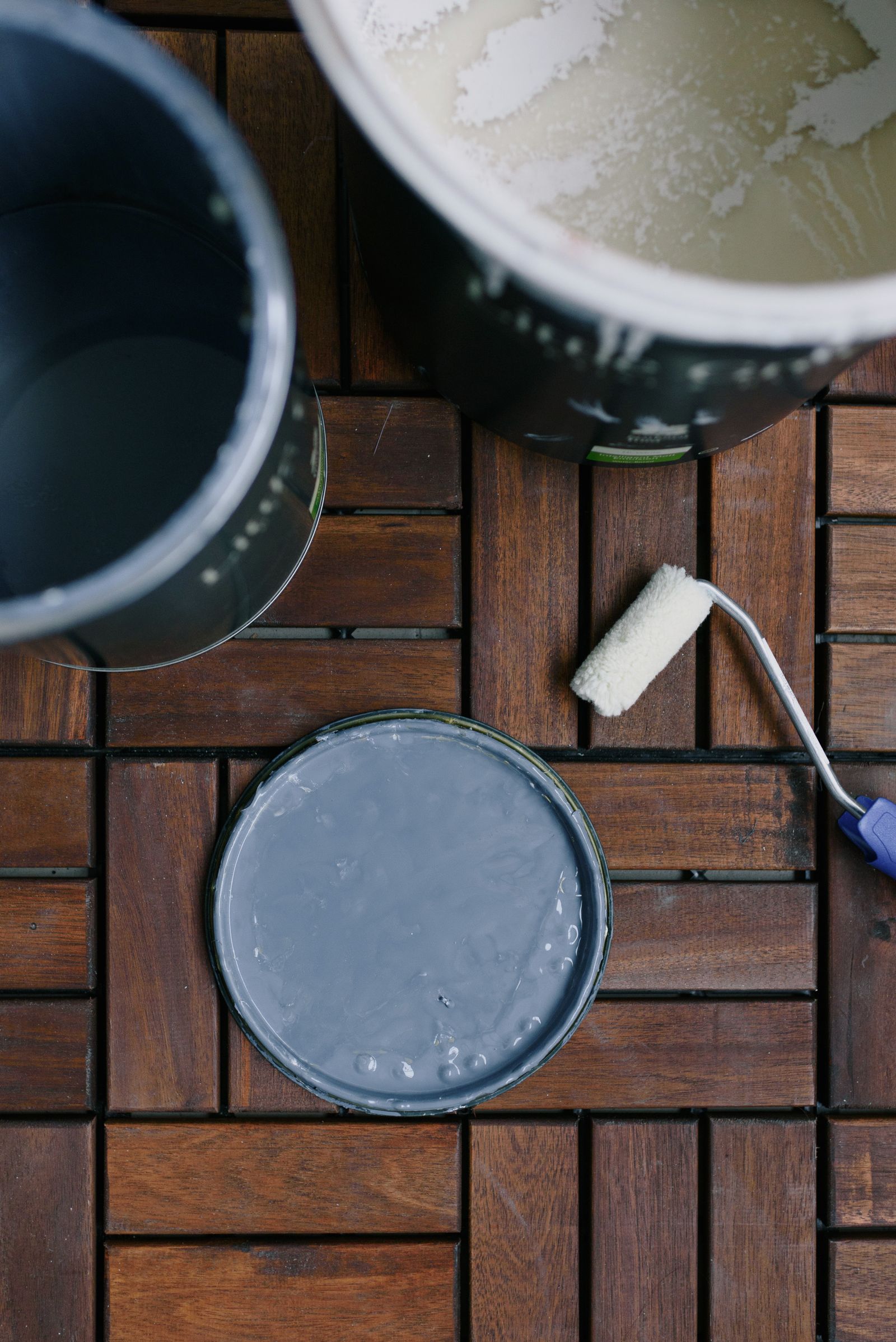 Open paint cans and a clean roller arranged on a wooden floor