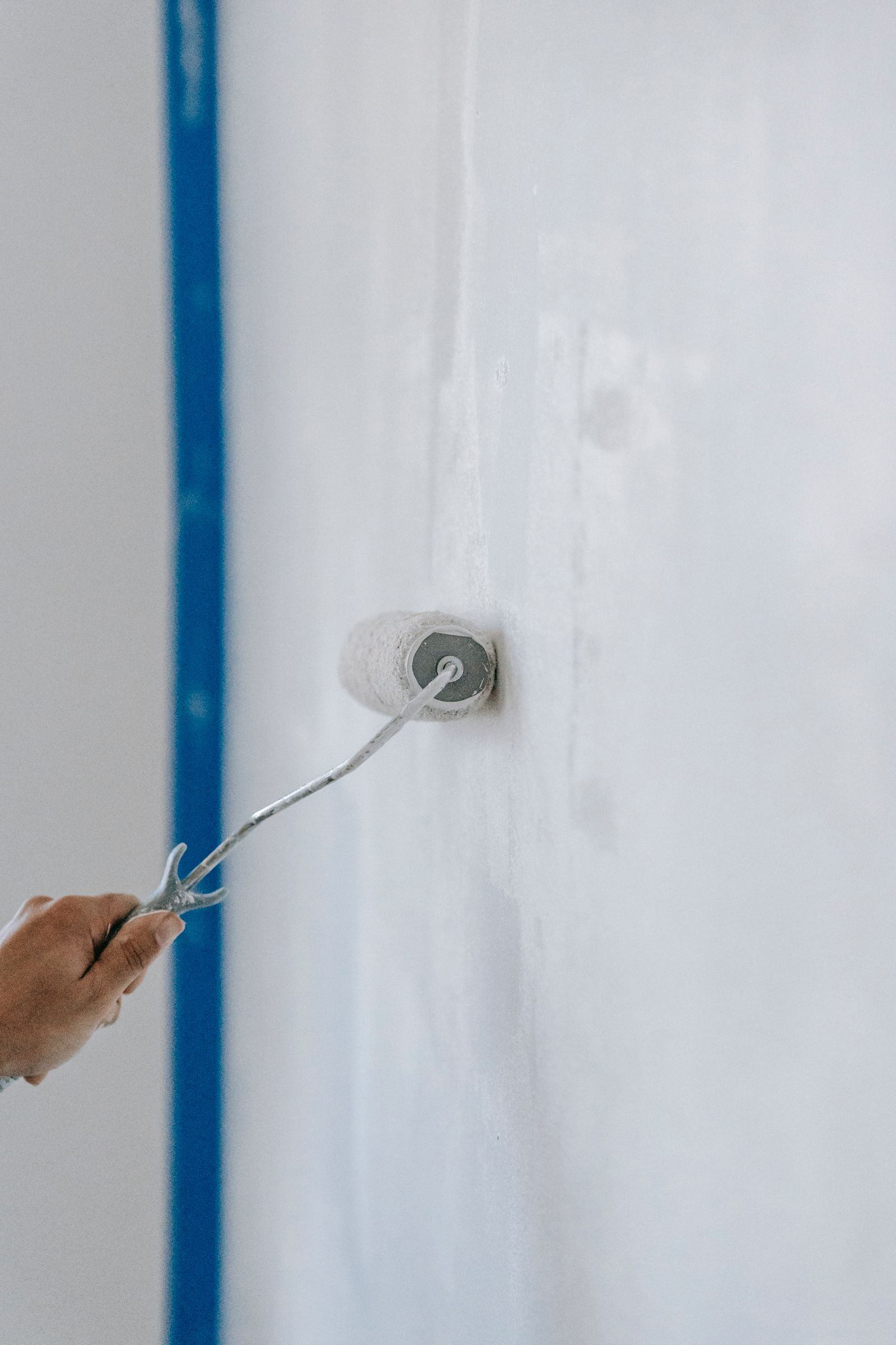 A person rolling white paint onto an interior wall