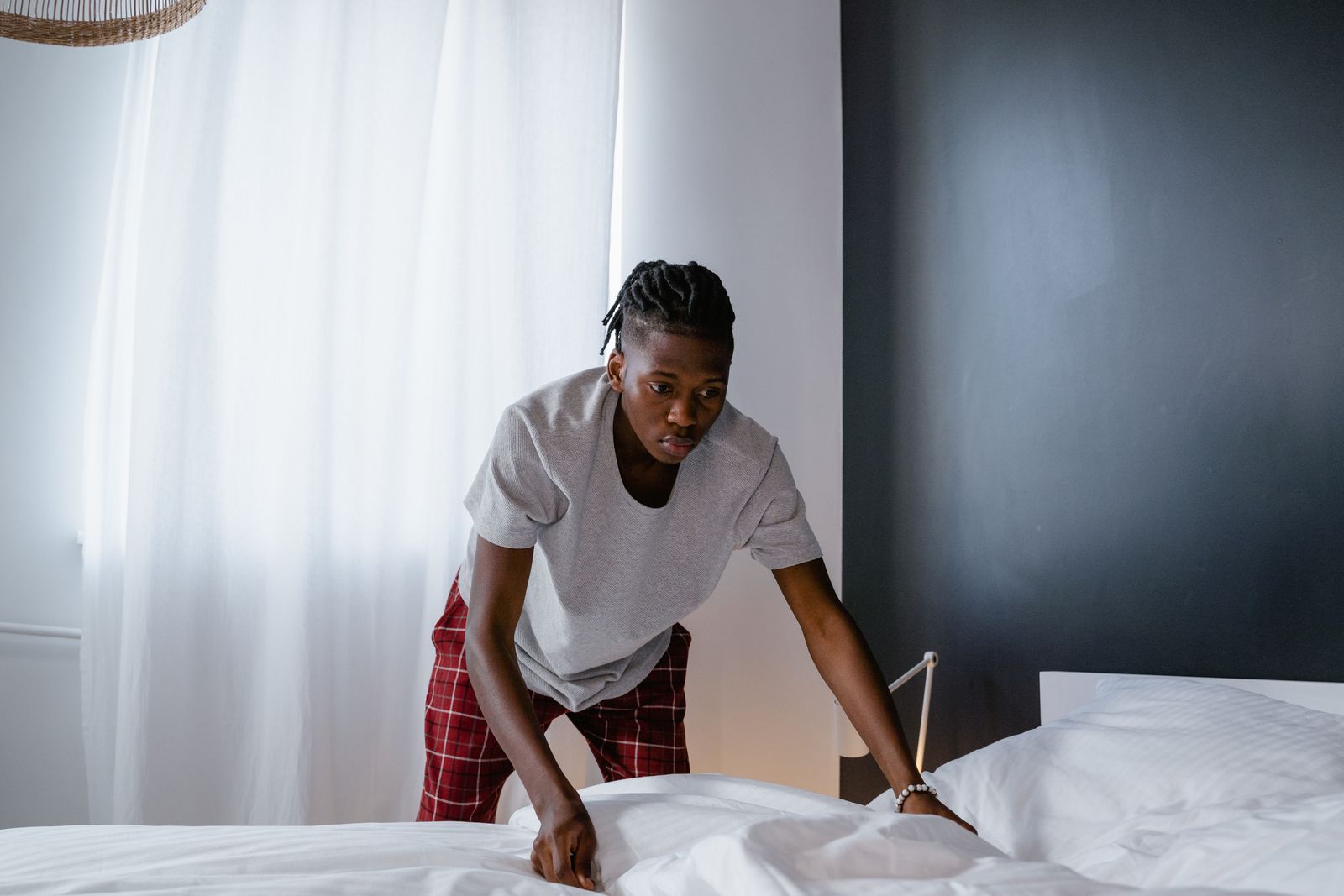 A person making a bed in a bright neutral bedroom