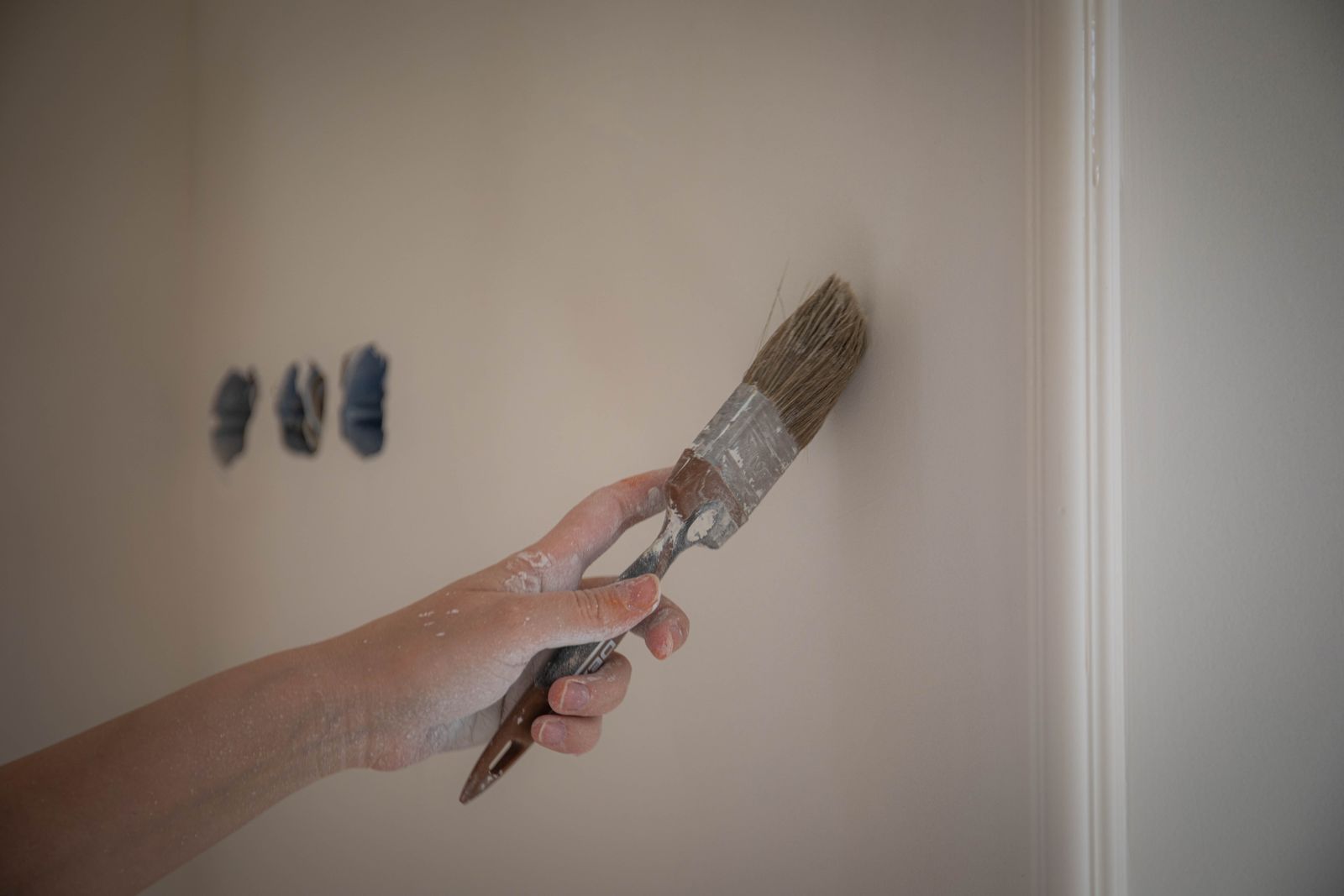 A hand uses an angled brush to paint a narrow wall edge beside interior trim