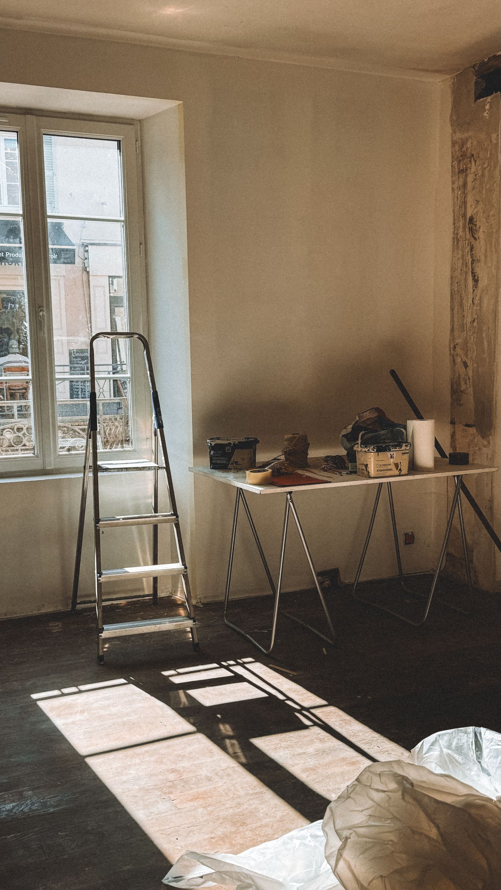A room under renovation with a step ladder and painting supplies staged near a wall