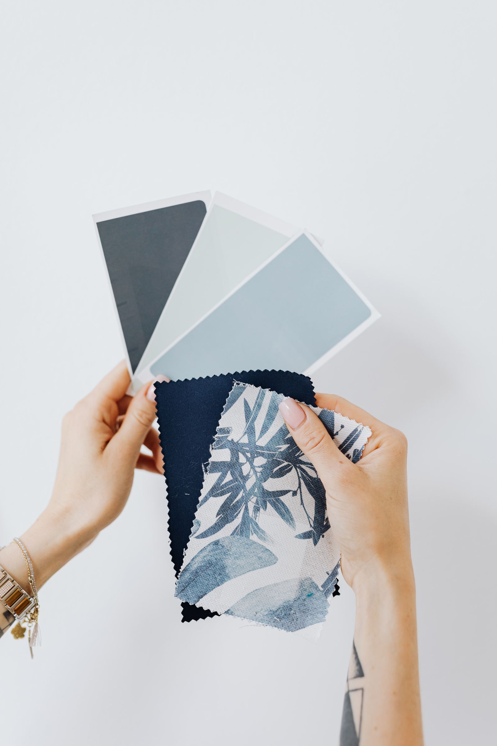Hands comparing blue and gray paint cards with blue patterned fabric