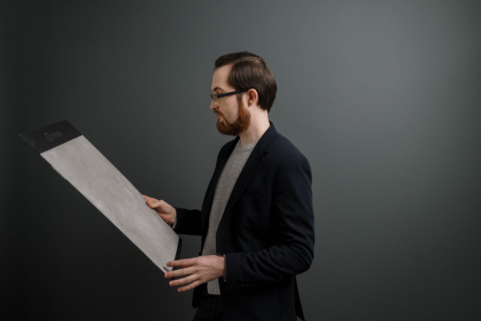 A person holding a large gray sample board against a dark painted wall
